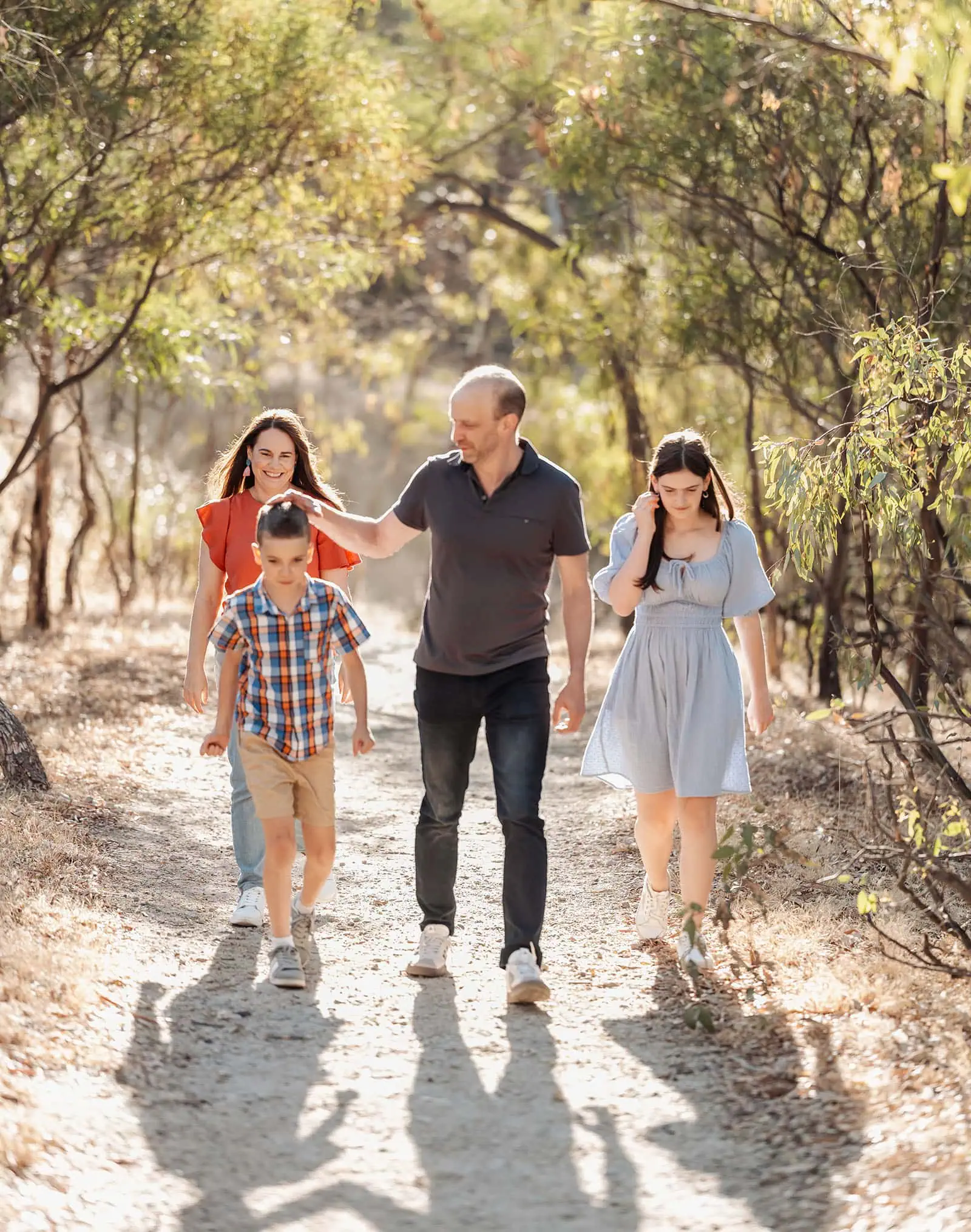 beautiful anstey hill family photoshoot 7 Family enjoying a sunny walk on a tree-lined path in nature.