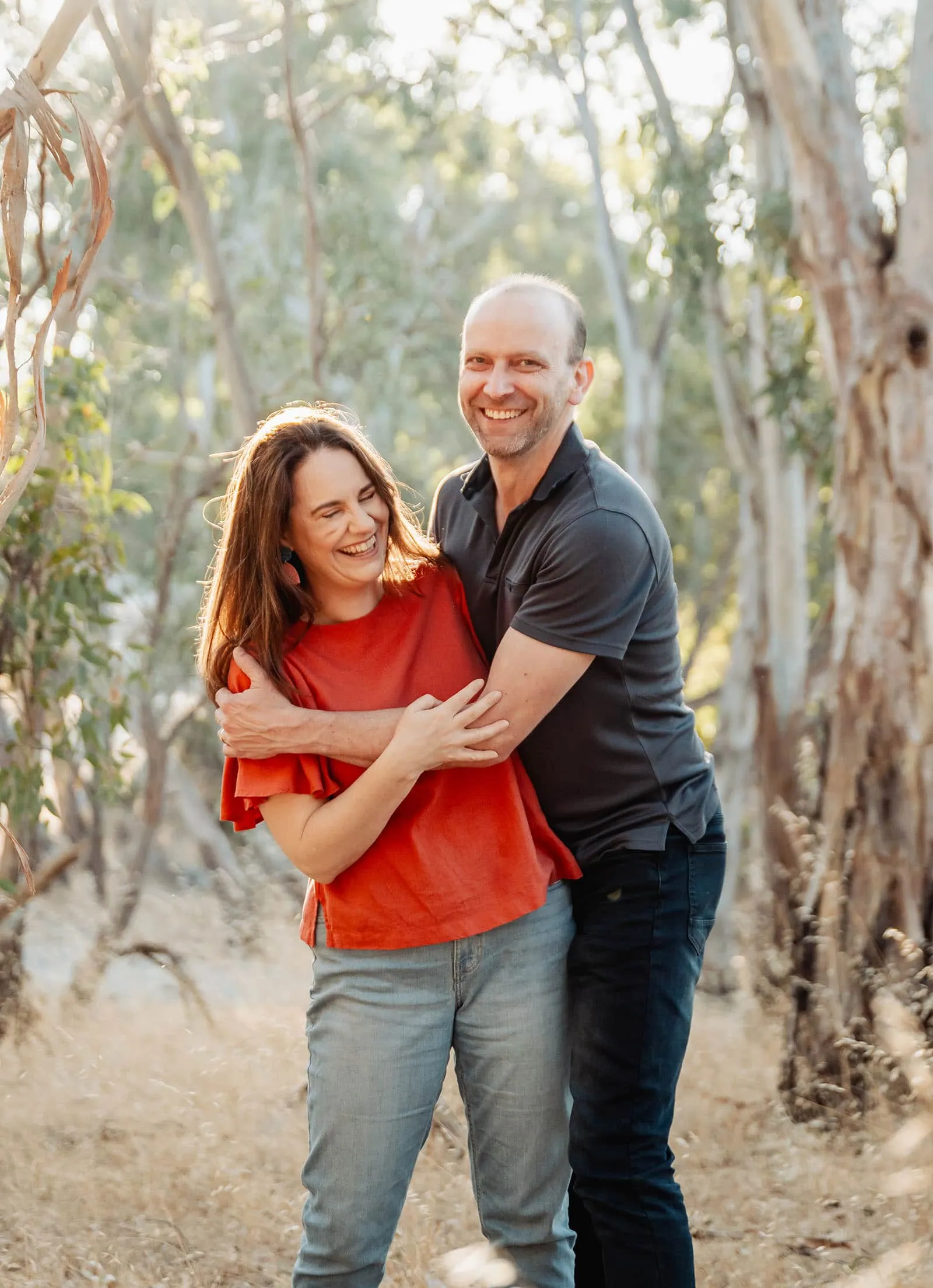beautiful anstey hill family photoshoot 21 Joyful couple embracing in a sunlit forest setting, exuding happiness and connection.