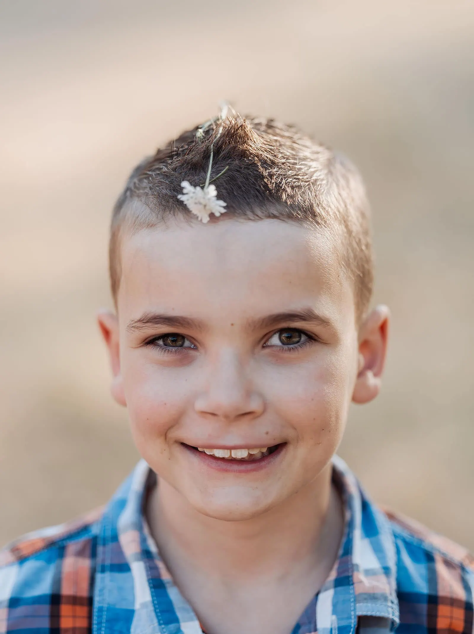 beautiful anstey hill family photoshoot 28 Smiling boy with plaid shirt and white flower in hair, cheerful and playful outdoors.