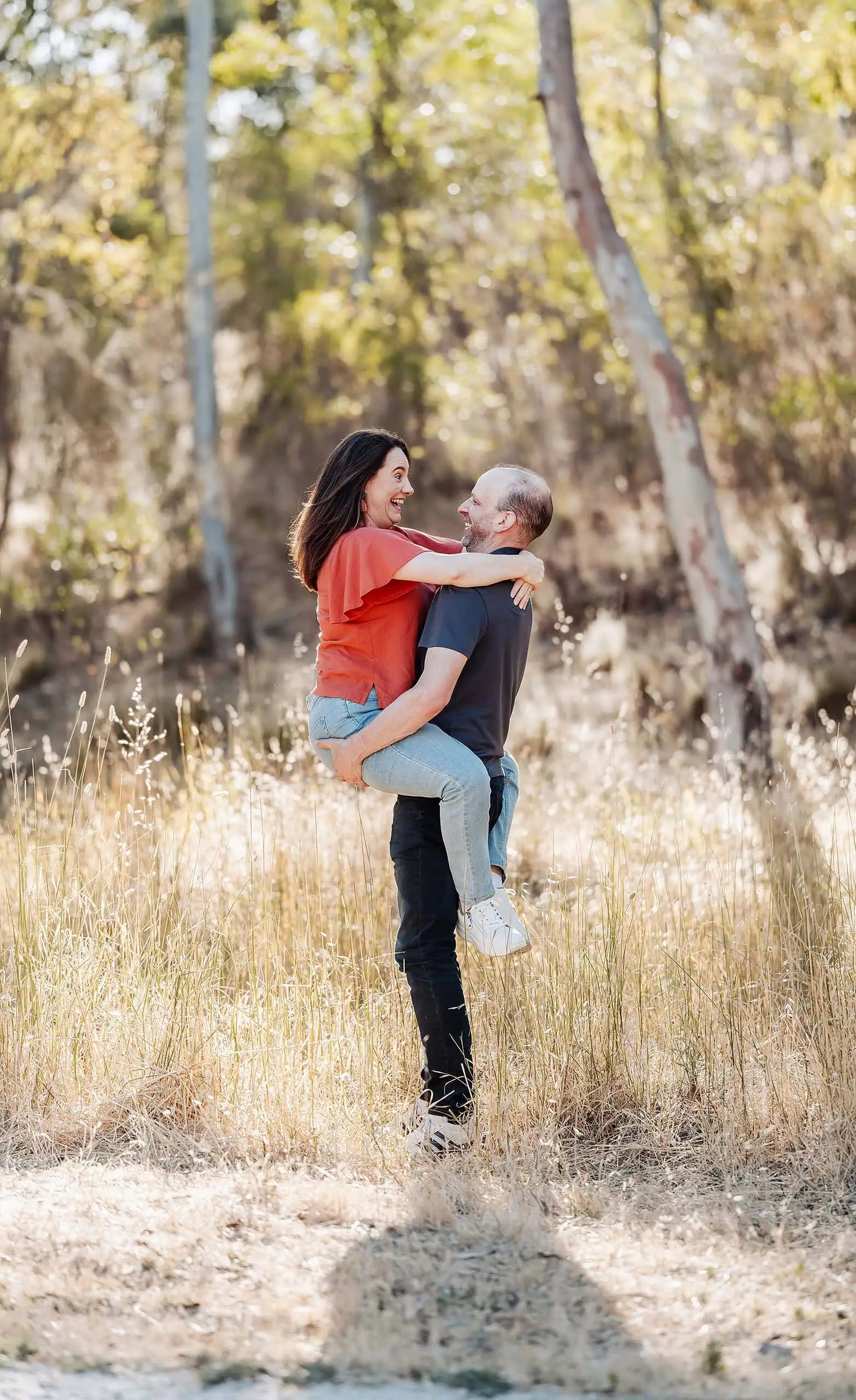 beautiful anstey hill family photoshoot 4 Happy couple embracing in a sunlit meadow, wearing bright clothing amidst nature.