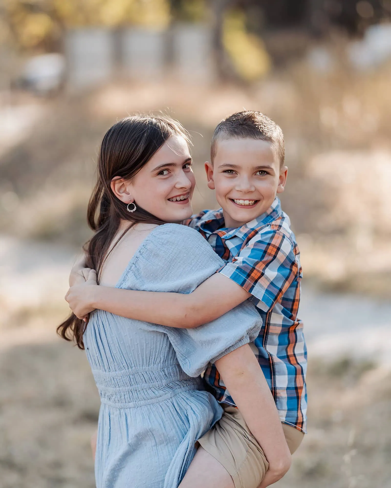 beautiful anstey hill family photoshoot 5 Siblings smiling outdoors in sunshine, girl in blue dress, boy in plaid shirt.