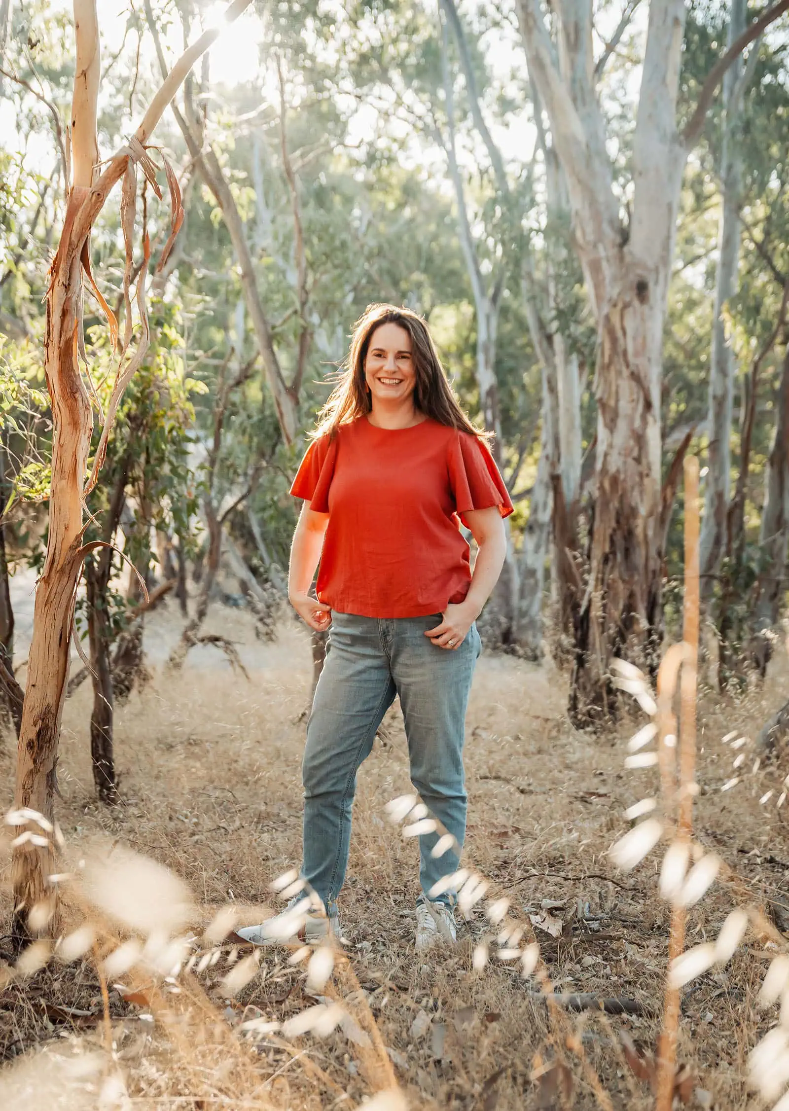 beautiful anstey hill family photoshoot 19 Woman in red blouse standing in serene forest with eucalyptus trees and sunlight.