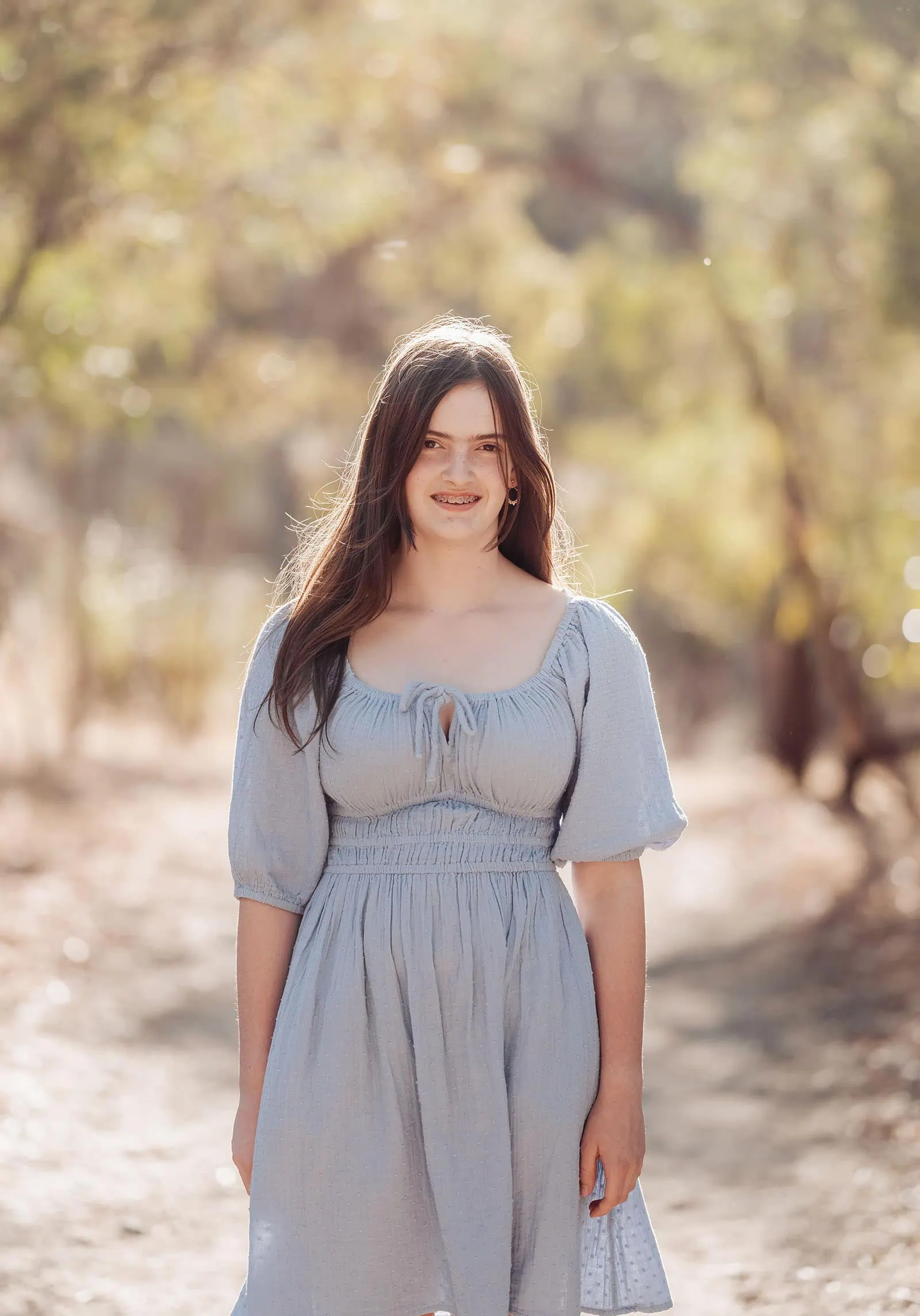 beautiful anstey hill family photoshoot 10 Young woman in blue dress smiling on sunlit path in park.