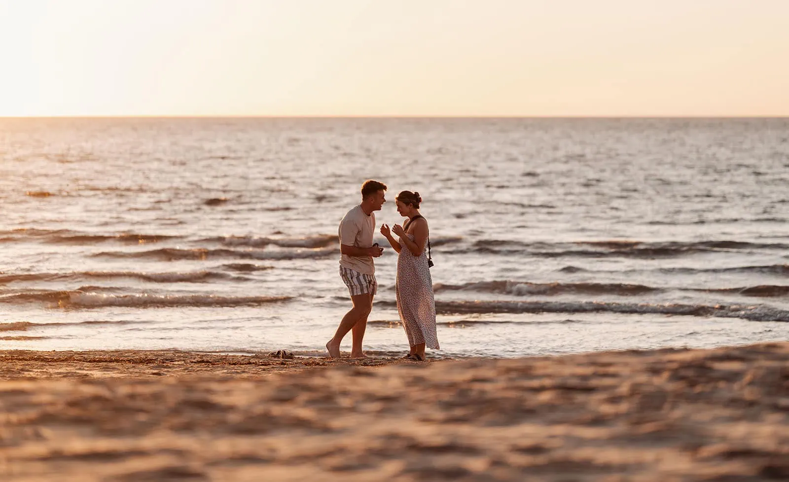 christies beach proposal – hollie & william 35 Couple embracing during golden hour on beach with ocean waves and sunset glow.