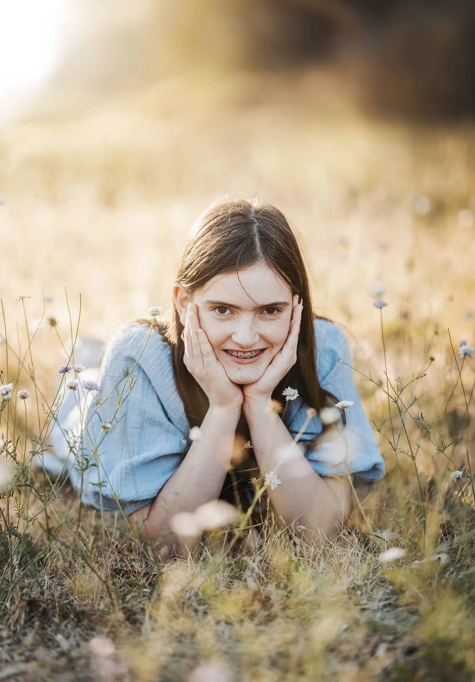 beautiful anstey hill family photoshoot 27 Girl relaxing in sunlit golden field, smiling with braces amid wildflowers.
