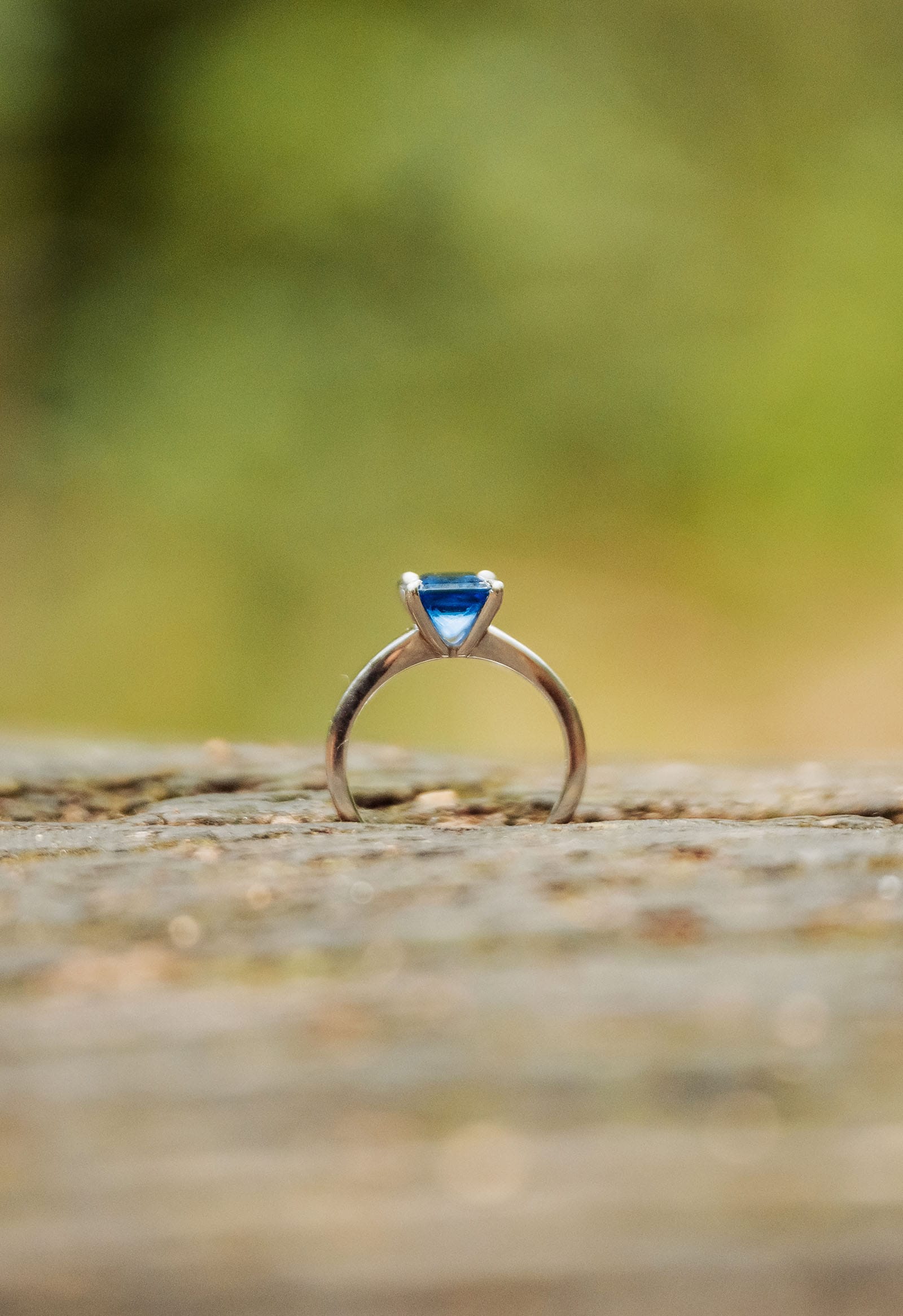botanic gardens wedding shoot - olivia & sean 27 Elegant ring with vivid blue triangular gemstone on platinum band against muted green background.