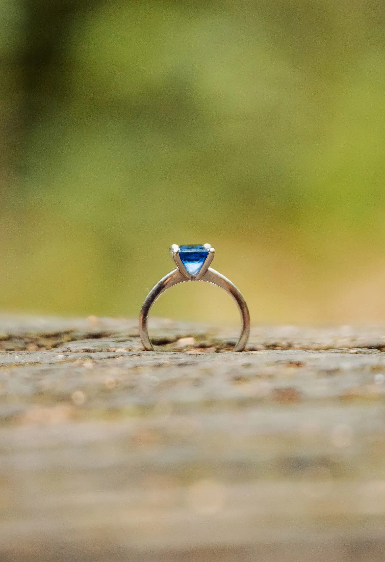 botanic gardens wedding shoot - olivia & sean 27 Elegant ring with vivid blue triangular gemstone on platinum band against muted green background.