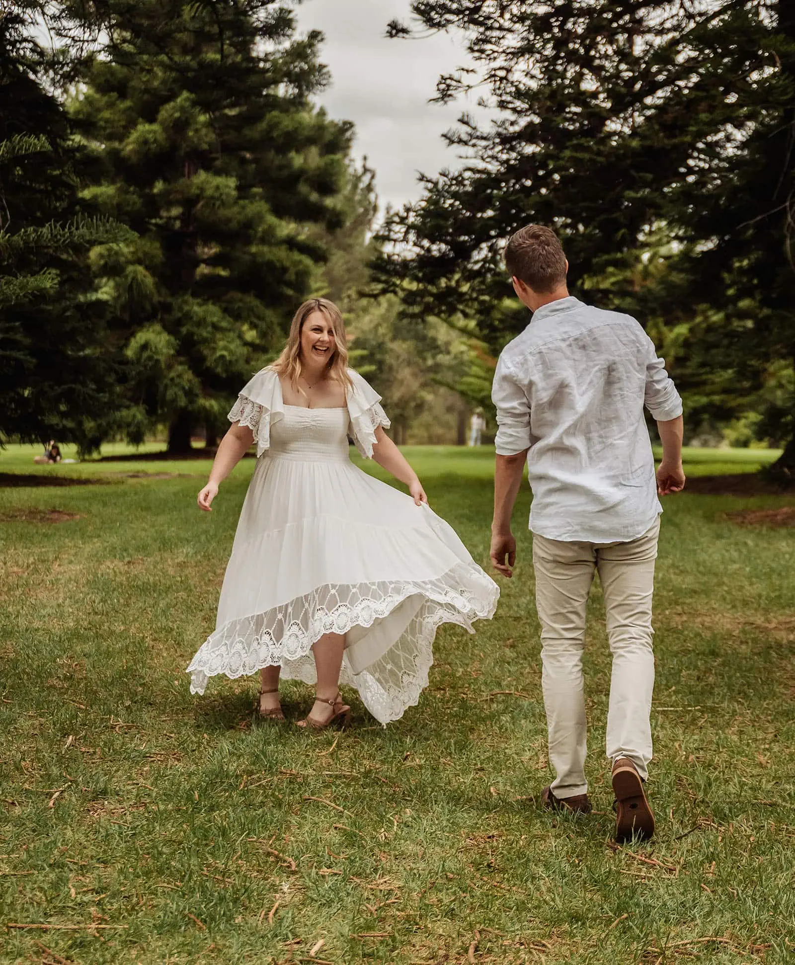 botanic gardens wedding shoot - olivia & sean 20 Joyful couple dancing in lush park setting with vibrant greenery and elegant attire.