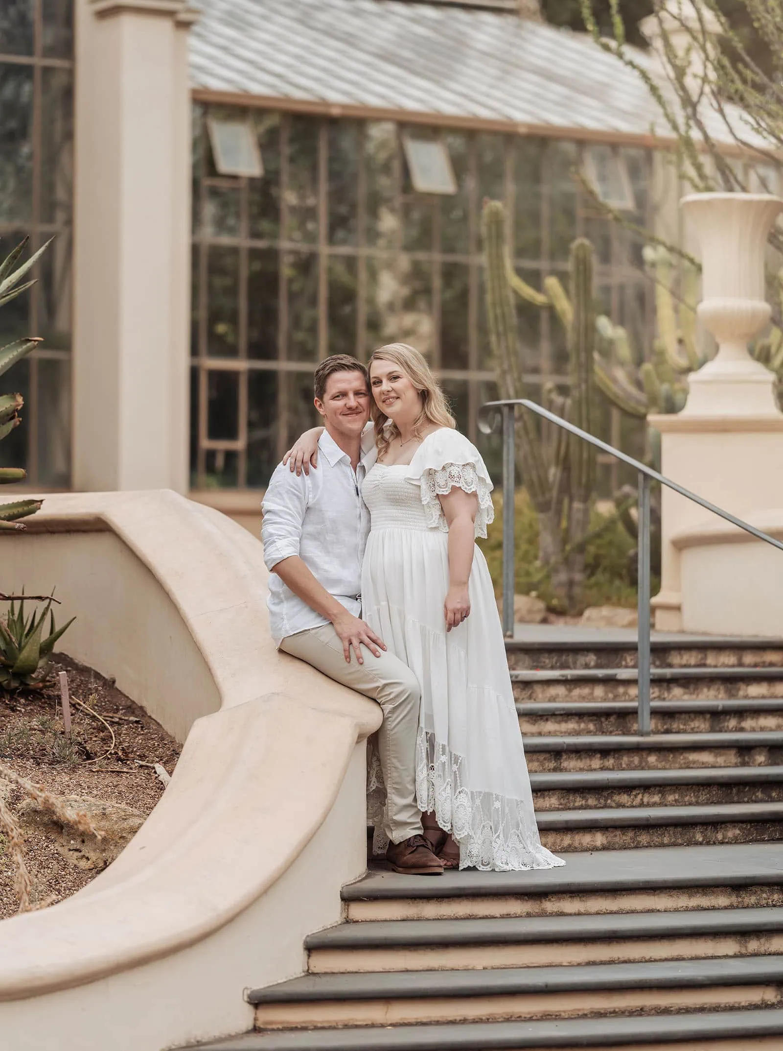 botanic gardens wedding shoot - olivia & sean 8 Couple posing romantically in garden steps near a glasshouse, surrounded by greenery.