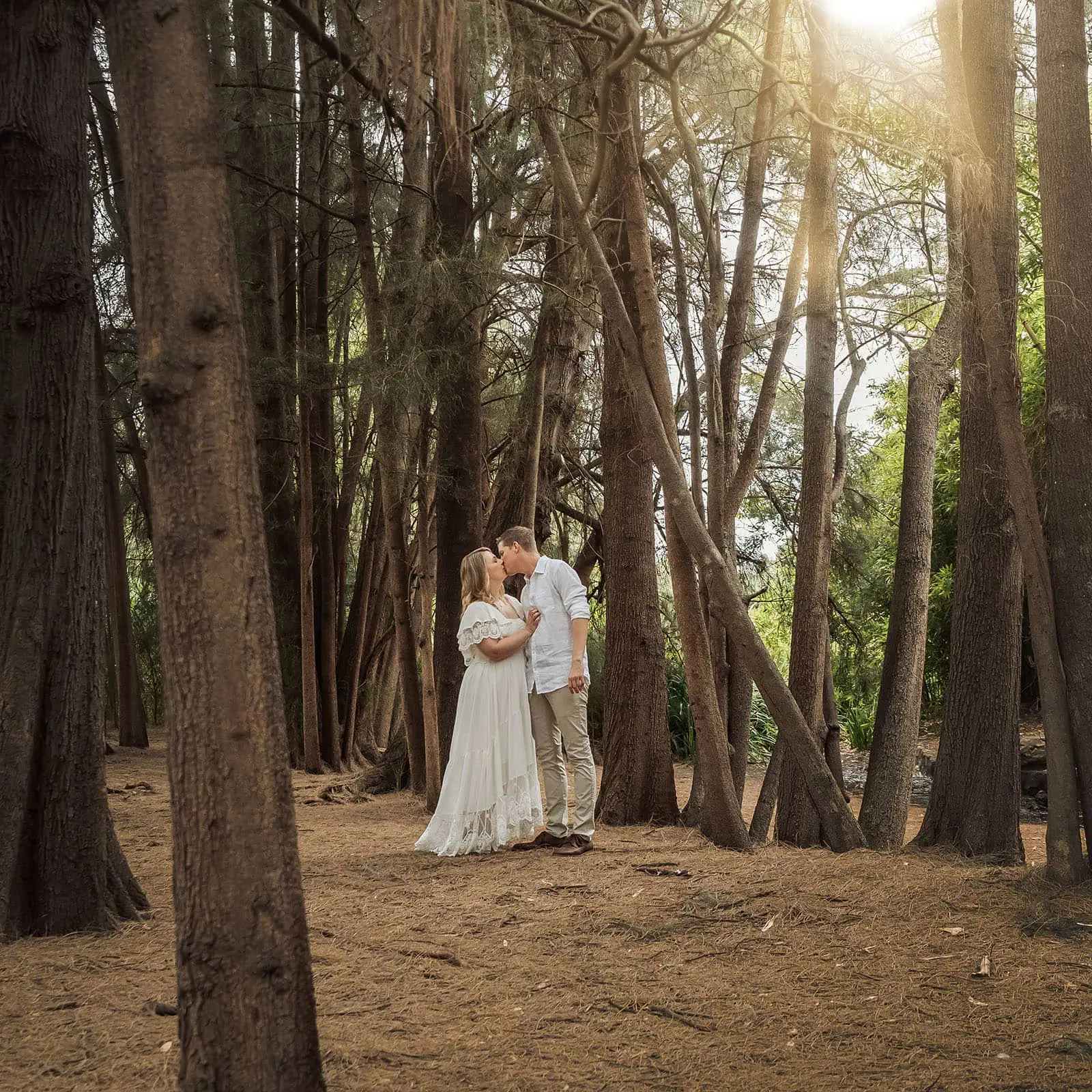 botanic gardens wedding shoot - olivia & sean 17 Couple kissing in sunlit forest, elegant attire, romantic ambiance.