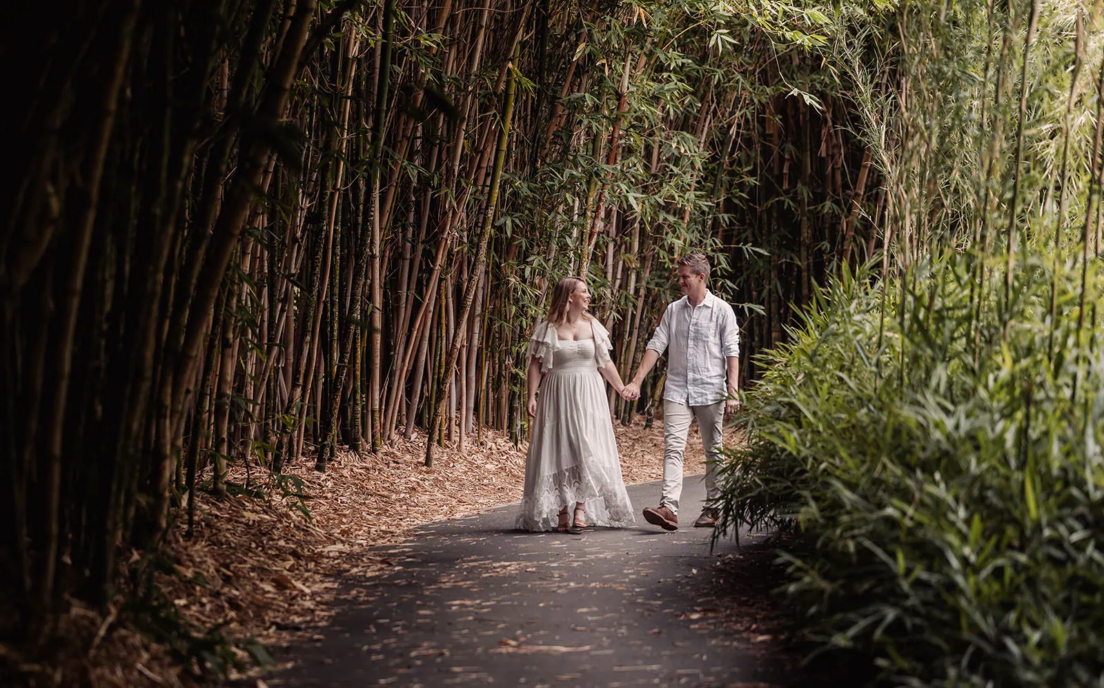 botanic gardens wedding shoot - olivia & sean 19 Couple strolling hand in hand through picturesque bamboo forest path in dappled sunlight.