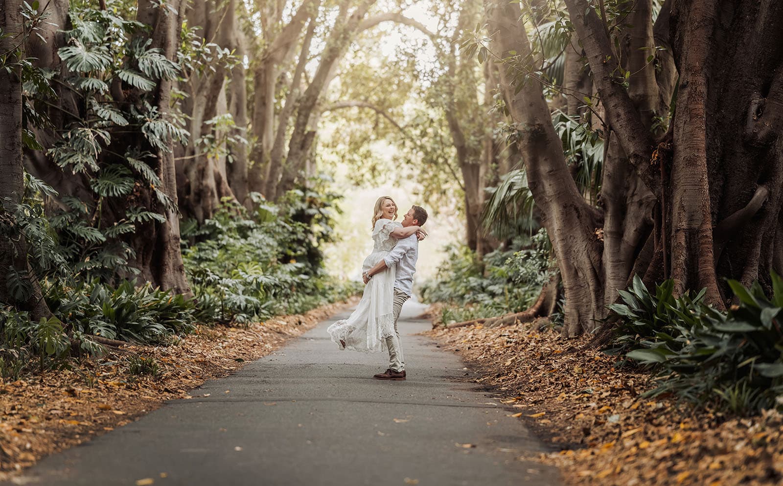 botanic gardens wedding shoot - olivia & sean 2 Romantic couple embracing on a forest path under sunlit trees.