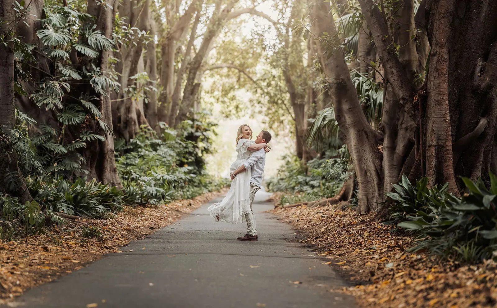 botanic gardens wedding shoot - olivia & sean 2 Romantic couple embracing on a forest path under sunlit trees.