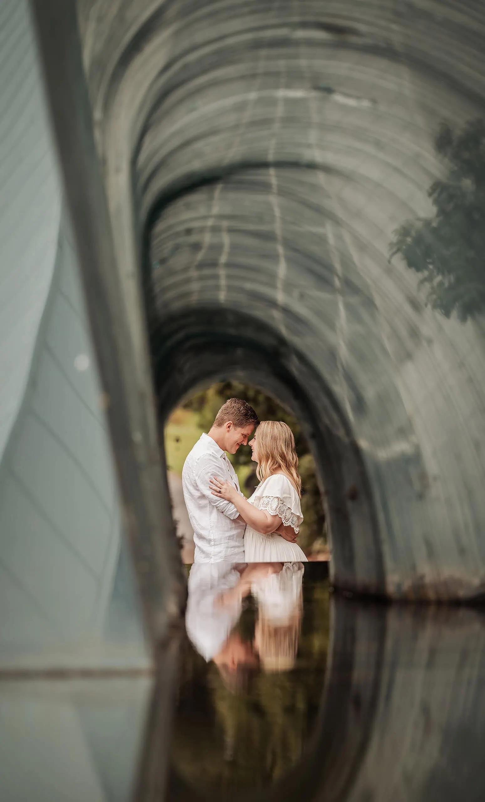 botanic gardens wedding shoot - olivia & sean 24 Couple embraces under translucent tunnel, reflecting in water with nature backdrop. Romantic, artistic scene.