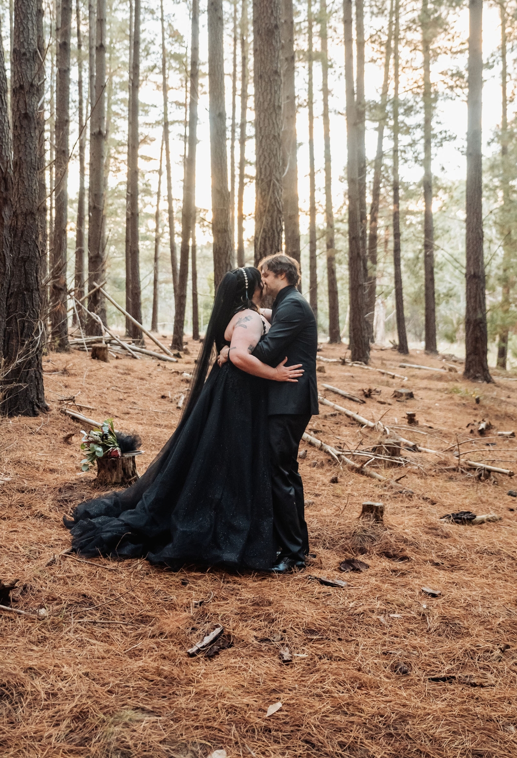 kuitpo forest metal themed wedding – erin & michael 14 Gothic black wedding couple kissing in sunlit pine forest elopement.