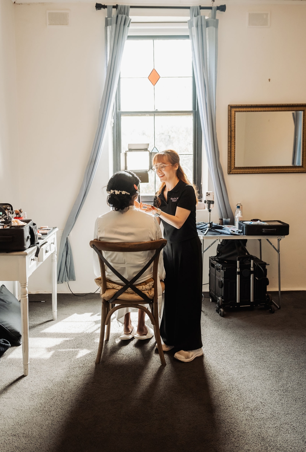manor wedding in basket range - methmini & aravinda 109 Makeup artist applying bridal makeup in a brightly lit room with elegant decor.