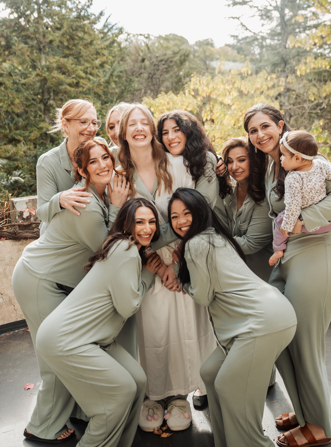 beautiful manor basket range wedding - sophie & theodore 91 Bride with bridesmaids in green pajamas, celebrating outdoors with smiles and affection.