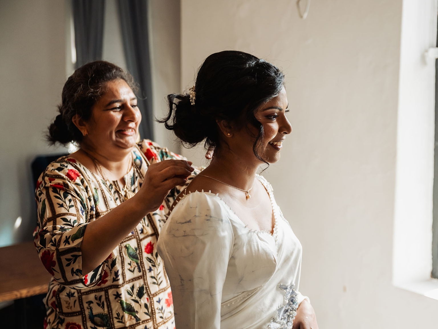 manor wedding in basket range - methmini & aravinda 115 Bride and friend share joyful preparation moment in elegantly decorated room.