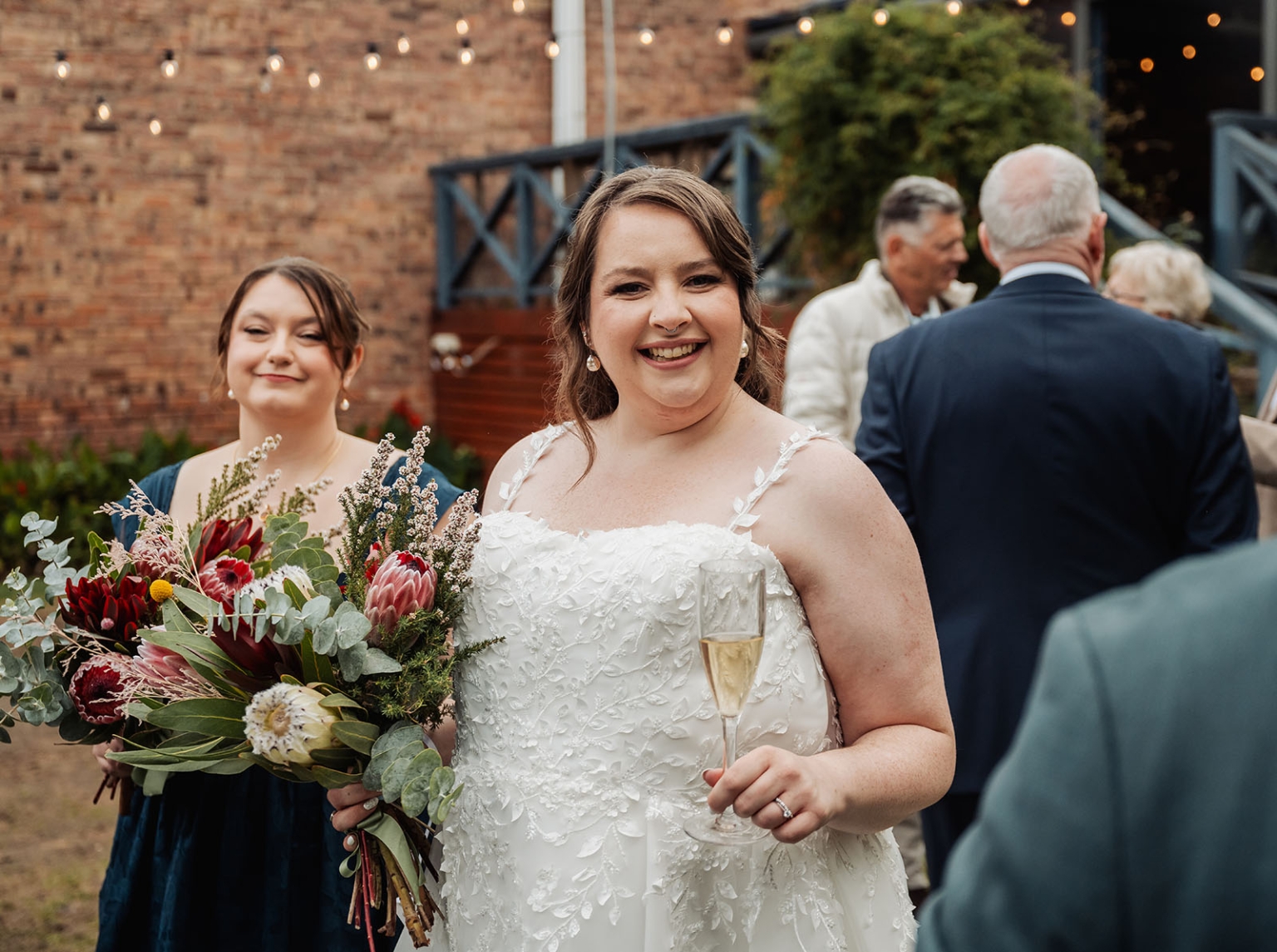 comida wedding - georgia & james 27 Bride celebrating with champagne, elegant lace gown, vibrant bouquet, rustic wedding ambiance.