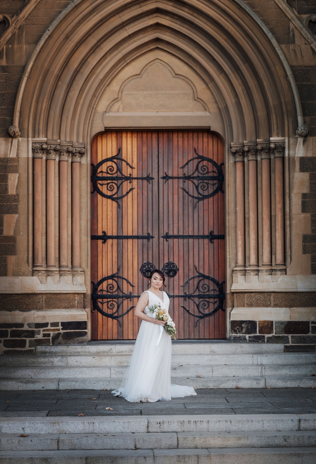 adelaide's st peter's cathedral wedding - irish & nick 3 Bride in white wedding gown with bouquet on Gothic church steps.