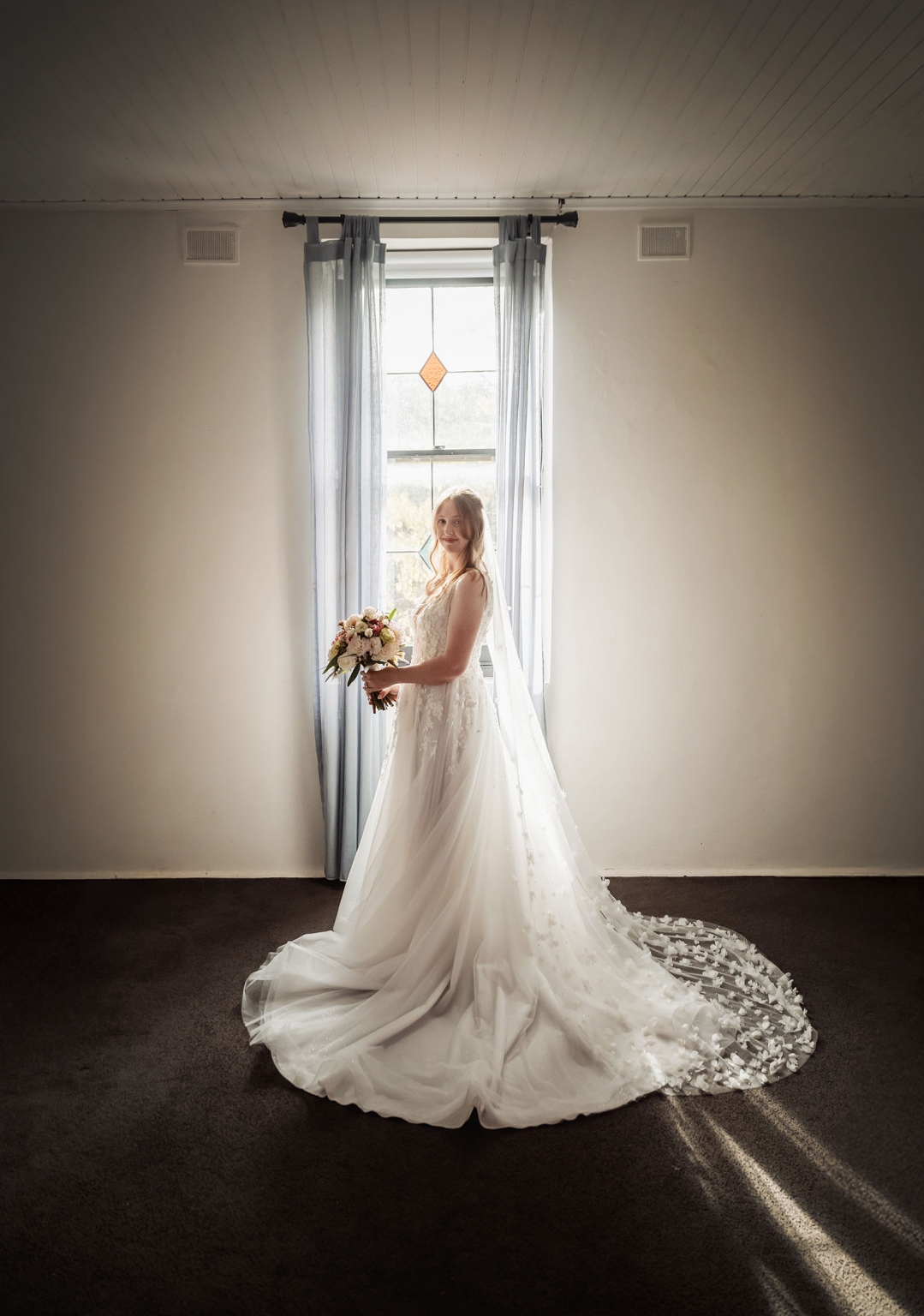 beautiful manor basket range wedding - sophie & theodore 96 Bride in elegant lace gown by window with pastel bouquet and soft lighting.