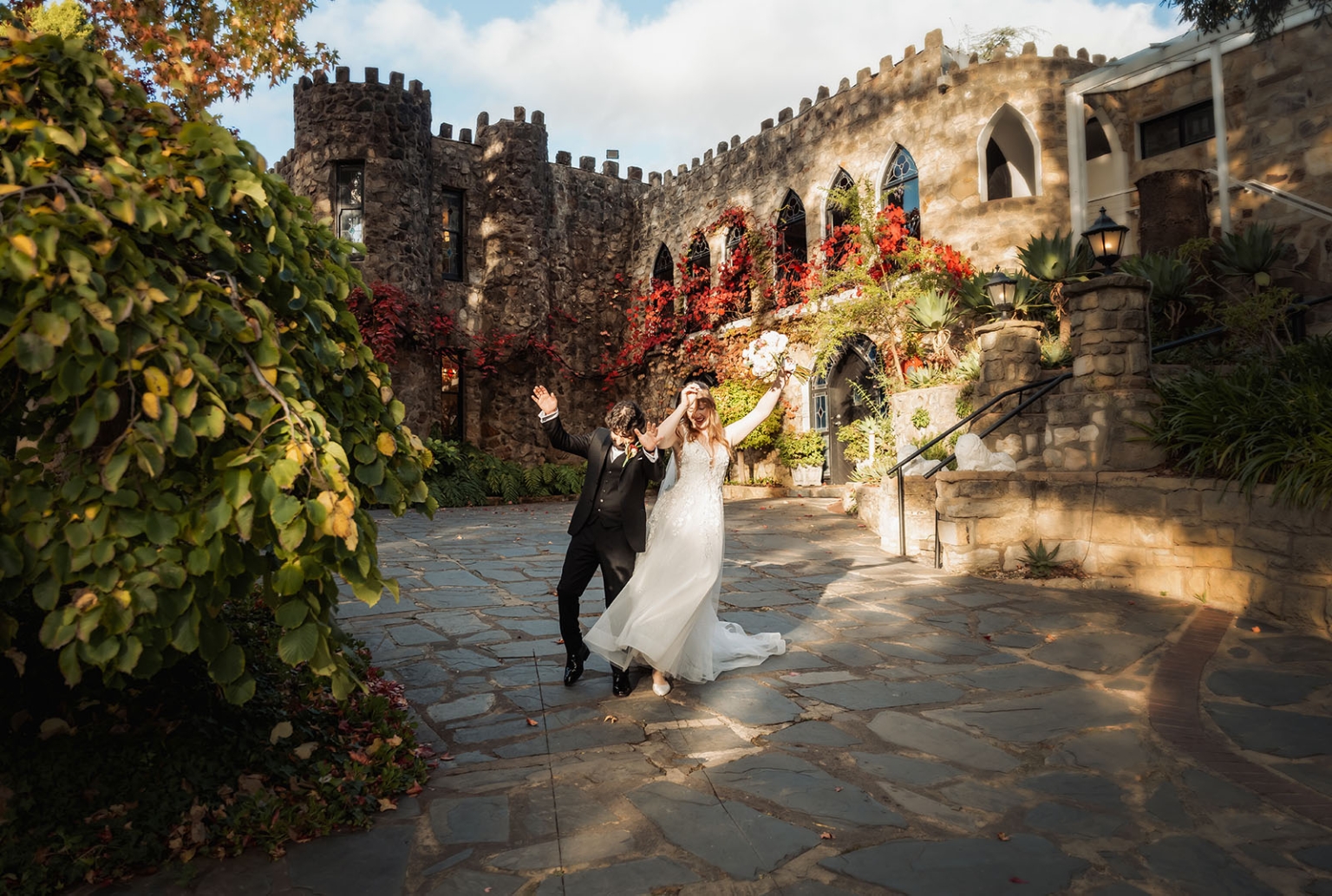 beautiful manor basket range wedding - sophie & theodore 120 Joyful couple celebrates wedding in elegant attire at a picturesque stone castle courtyard.