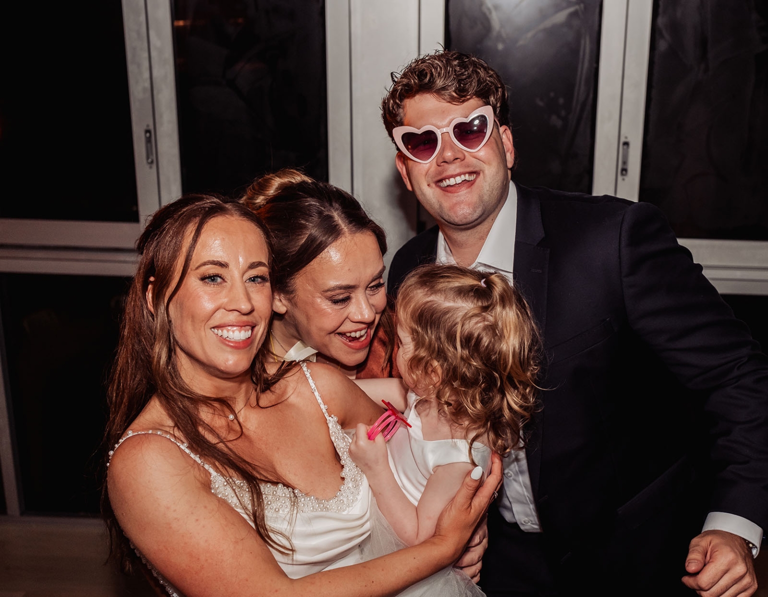 the lane vineyard wedding - caitlyn & craig 139 Joyful family celebration featuring a woman, child in white dresses, man in suit with heart-shaped sunglasses.