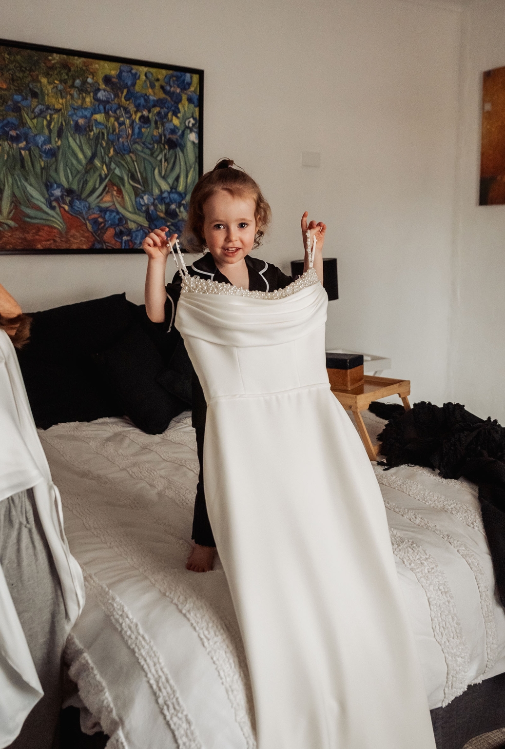 the lane vineyard wedding - caitlyn & craig 79 Child plays dress-up, holding large white satin dress in cozy, art-filled bedroom.