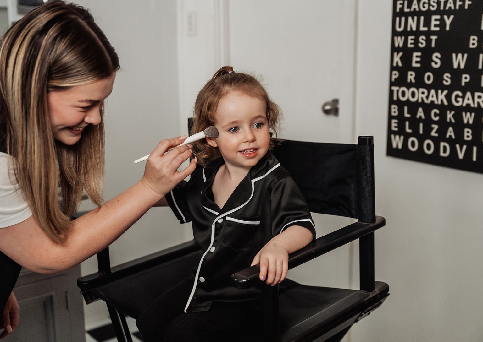 the lane vineyard wedding - caitlyn & craig 76 Woman applying makeup to child in directors chair, cozy room setting.