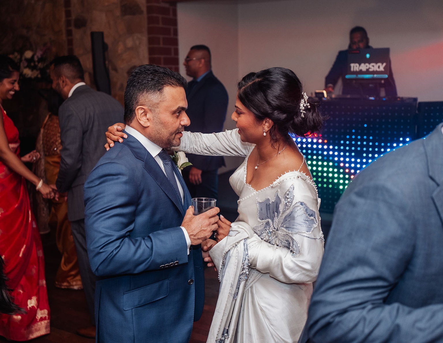manor wedding in basket range - methmini & aravinda 174 Elegant couple converses at a lively celebration with DJ TRAPSICK, wearing formal attire.