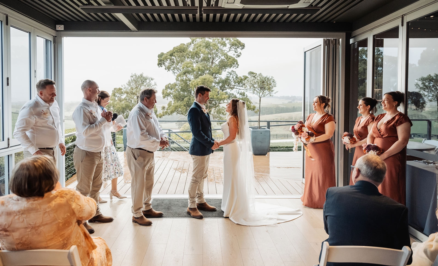 the lane vineyard wedding - caitlyn & craig 123 Modern indoor wedding with scenic view, bride in white, navy-suited groom, rust bridesmaids.