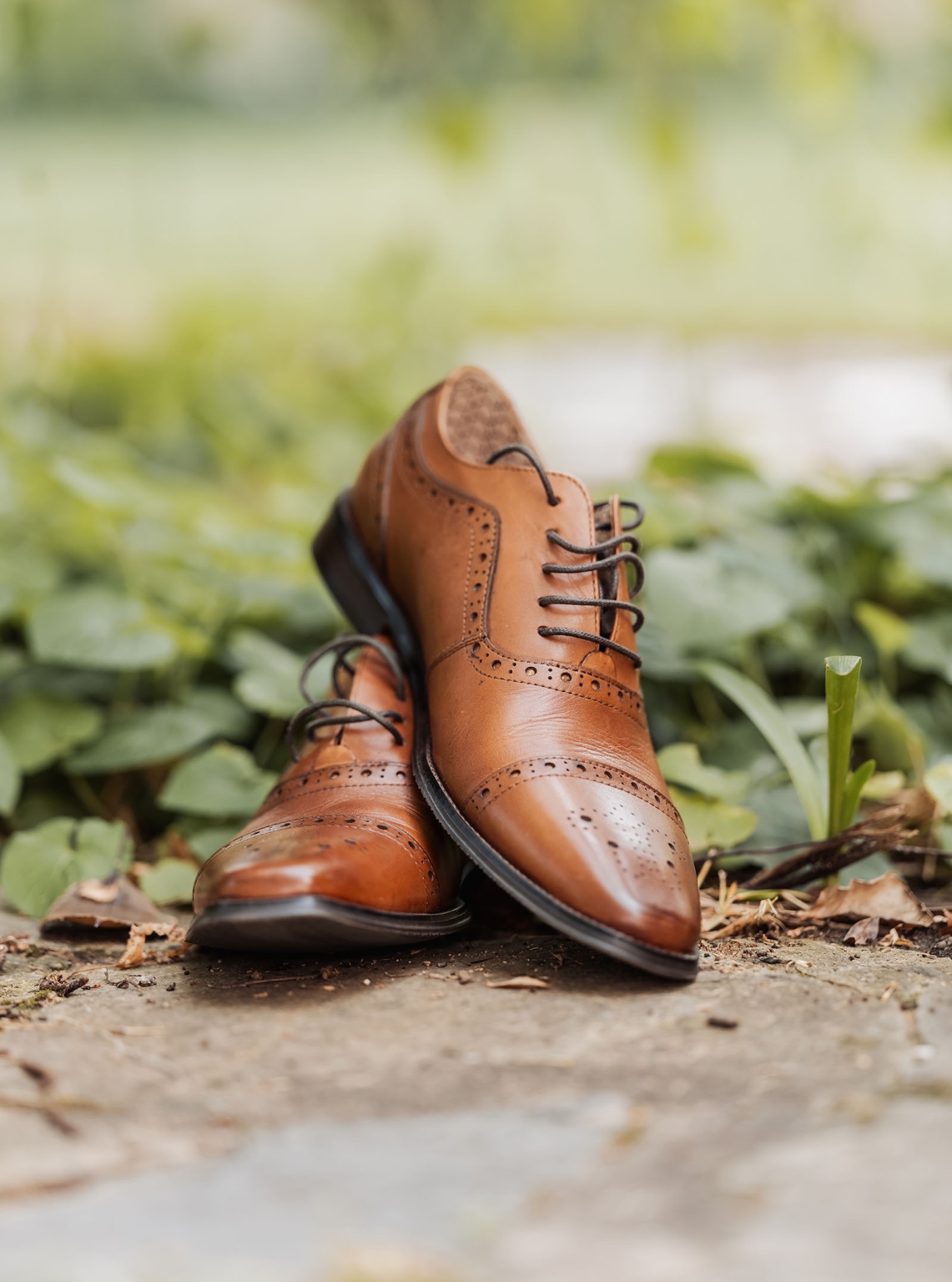 manor wedding in basket range - methmini & aravinda 95 Stylish brown leather brogues on stone with greenery, showcasing elegant design and craftsmanship.