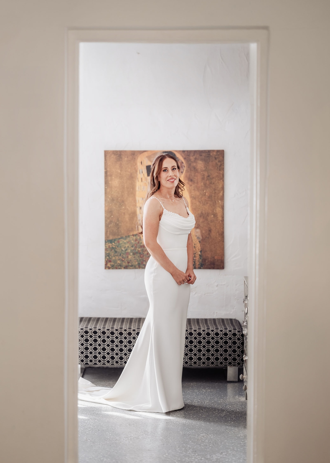 the lane vineyard wedding - caitlyn & craig 95 Elegant woman in white gown framed by doorway, smiling softly in a serene, artful setting.