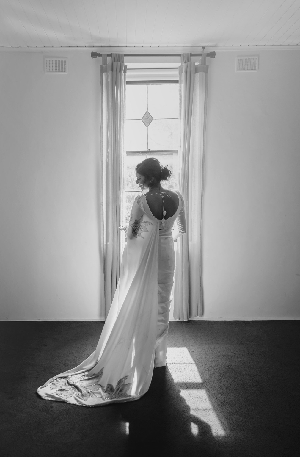 manor wedding in basket range - methmini & aravinda 117 Elegant woman in traditional saree by window, black-and-white portrait.