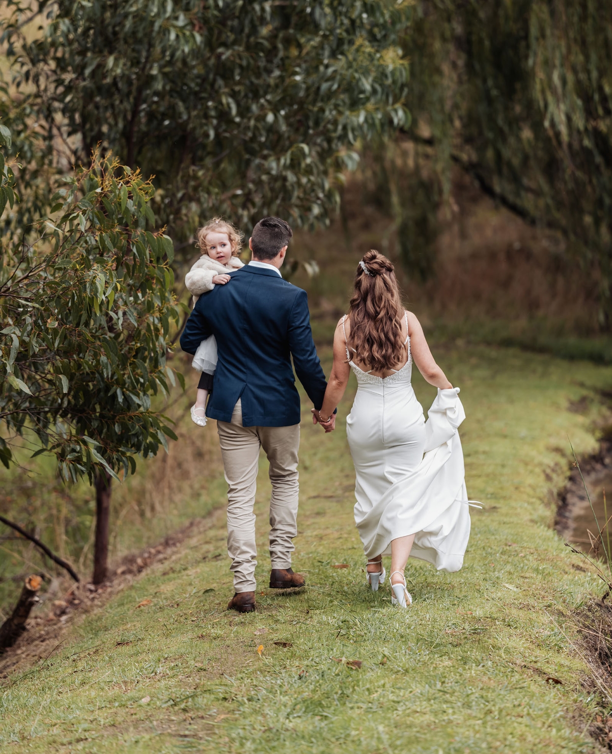 the lane vineyard wedding - caitlyn & craig 104 Newlyweds and child walking in nature, celebrating love and family connections.