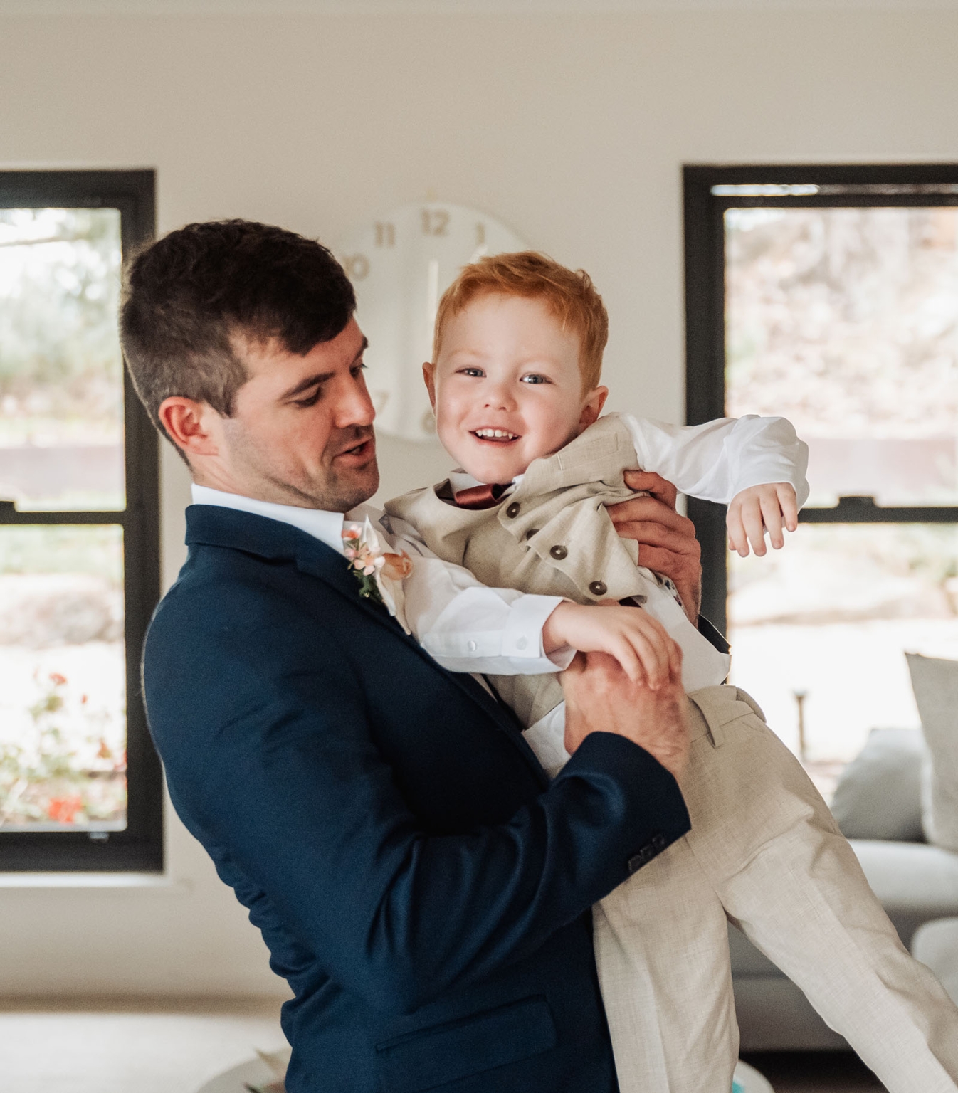 the lane vineyard wedding - caitlyn & craig 69 Man in blue suit joyfully holding red-haired boy in beige suit at formal event.
