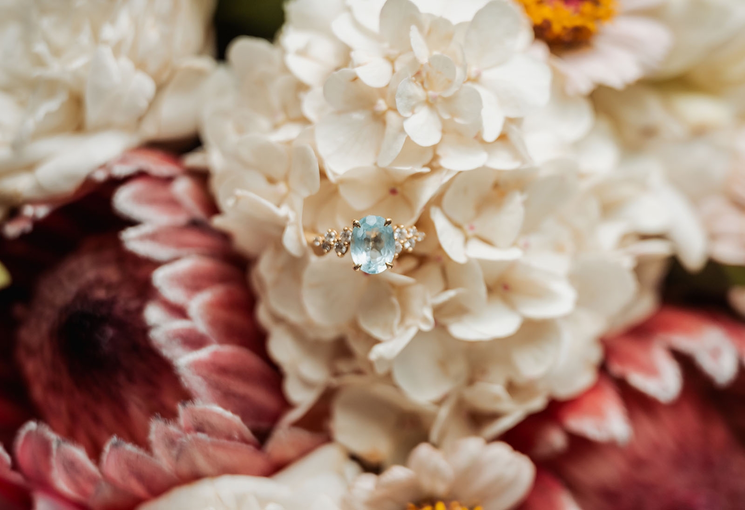 beautiful manor basket range wedding - sophie & theodore 88 Elegant ring and hydrangeas with protea flowers; aquamarine gemstone in floral arrangement.