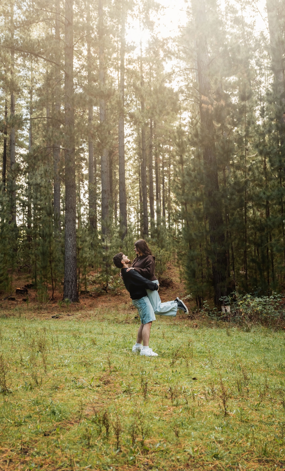 cabn at kuitpo forest proposal - tamsyn & blake 24 Couple playing in sunlit forest, surrounded by tall pine trees and lush greenery.
