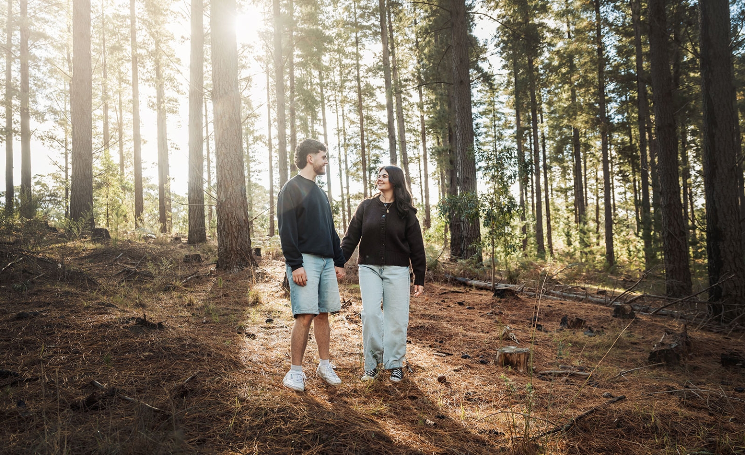 cabn at kuitpo forest proposal - tamsyn & blake 32 Couple walking in tranquil forest with sunlight filtering through tall pine trees.