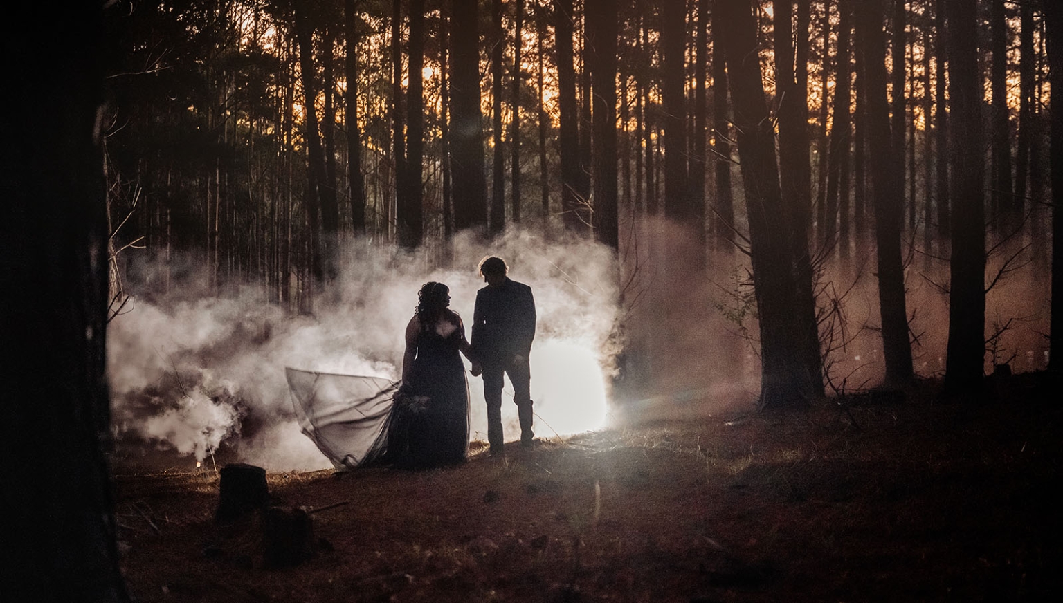 kuitpo forest metal themed wedding – erin & michael 32 Forest wedding silhouette couple holding hands in smoky sunset woods.