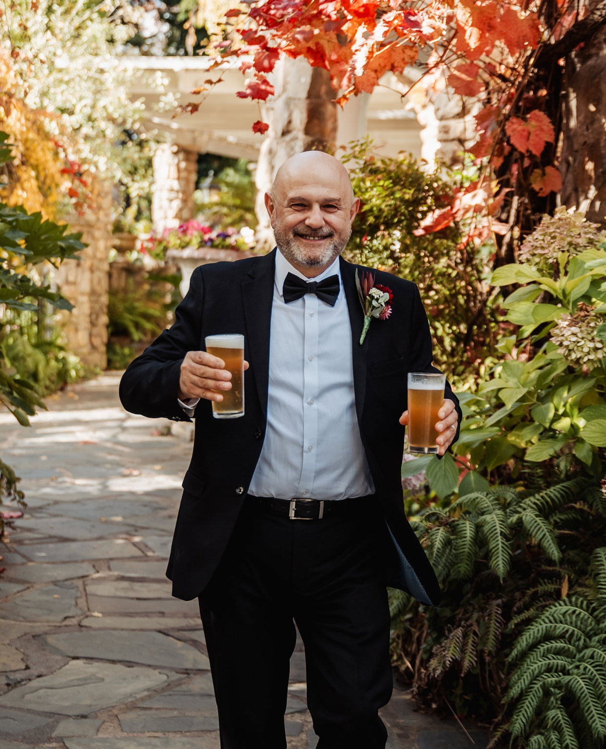 beautiful manor basket range wedding - sophie & theodore 87 Dapper man in suit with beer, smiling in autumn garden setting.