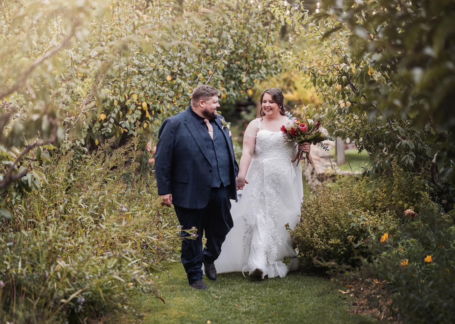 comida wedding - georgia & james 37 Joyful couple walking through lush garden on wedding day, surrounded by vibrant greenery.