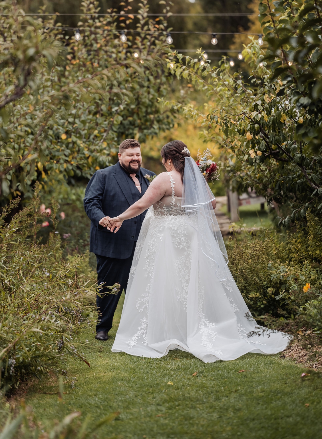 comida wedding - georgia & james 28 Bride and groom in lush garden, celebrating wedding under string lights.