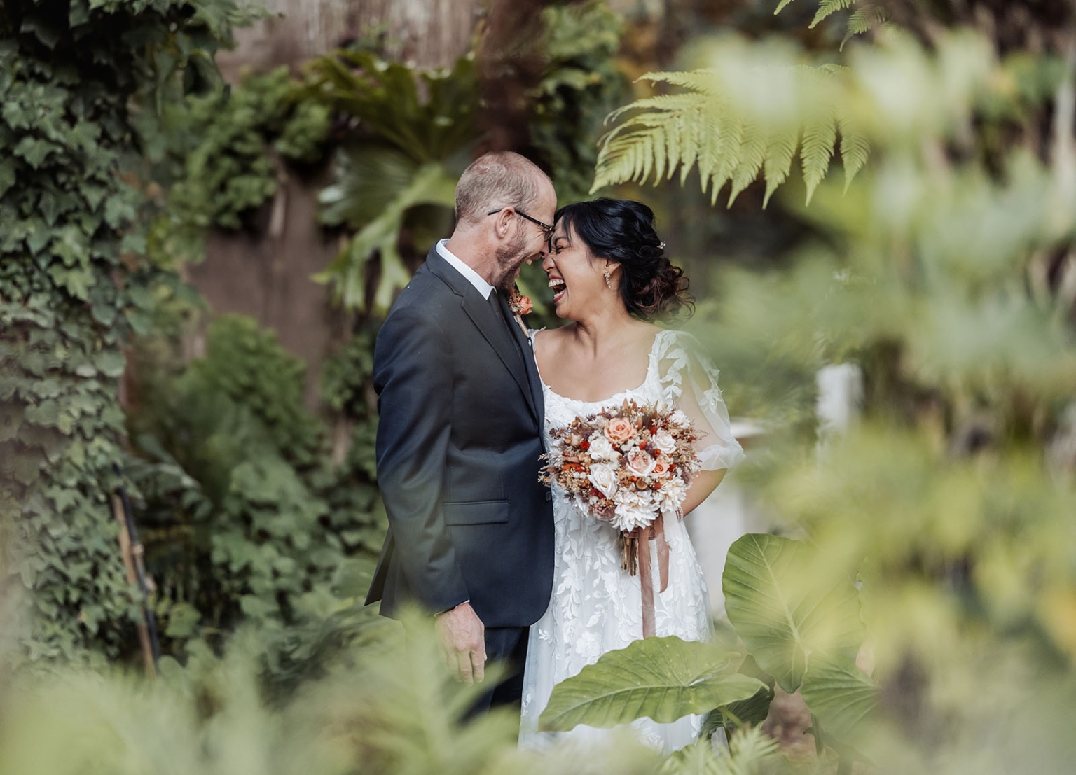 adelaide hills wedding at the manor - jo & dan 33 Joyful bride and groom laughing in lush garden wedding portrait.