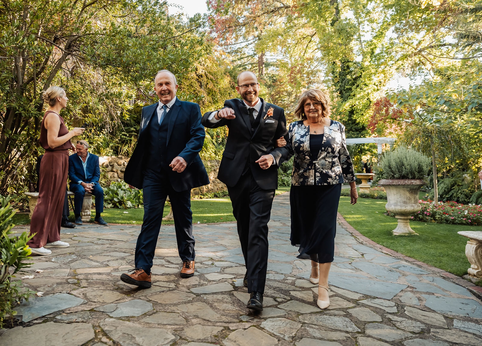 adelaide hills wedding at the manor - jo & dan 17 Joyful groom walks with family at elegant outdoor garden wedding ceremony.