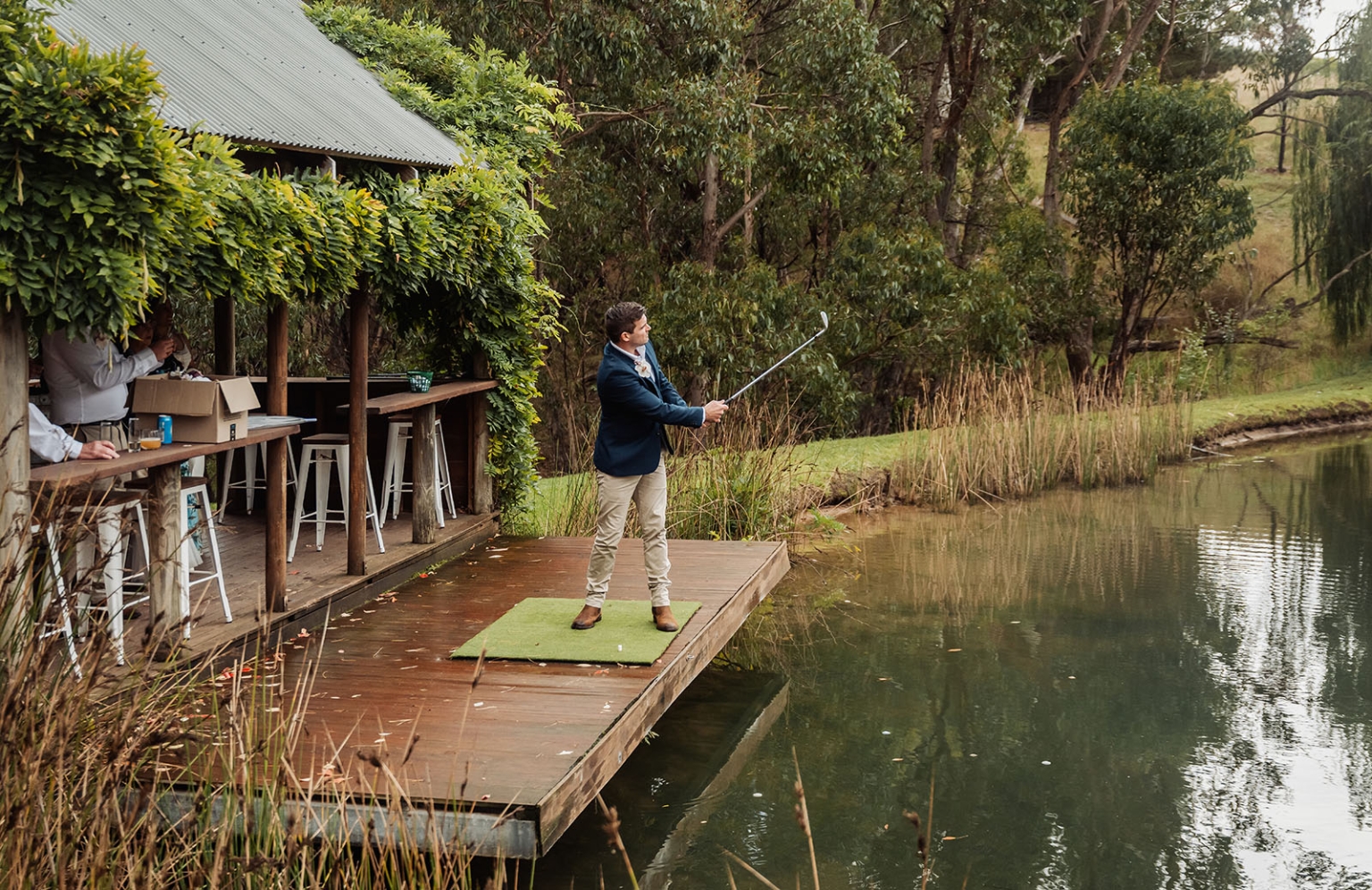 the lane vineyard wedding - caitlyn & craig 109 Man golfing on lakeside deck among lush greenery.