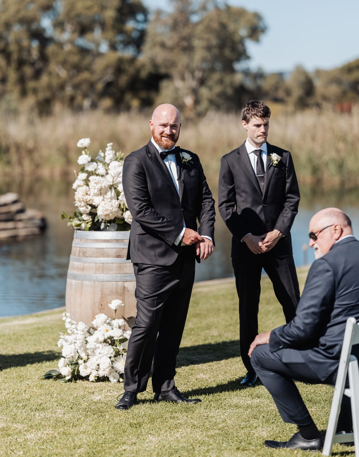 lloyd brothers wedding - dajana & tom 7 Groom and groomsman at outdoor wedding near water, formal suits, serene setting.