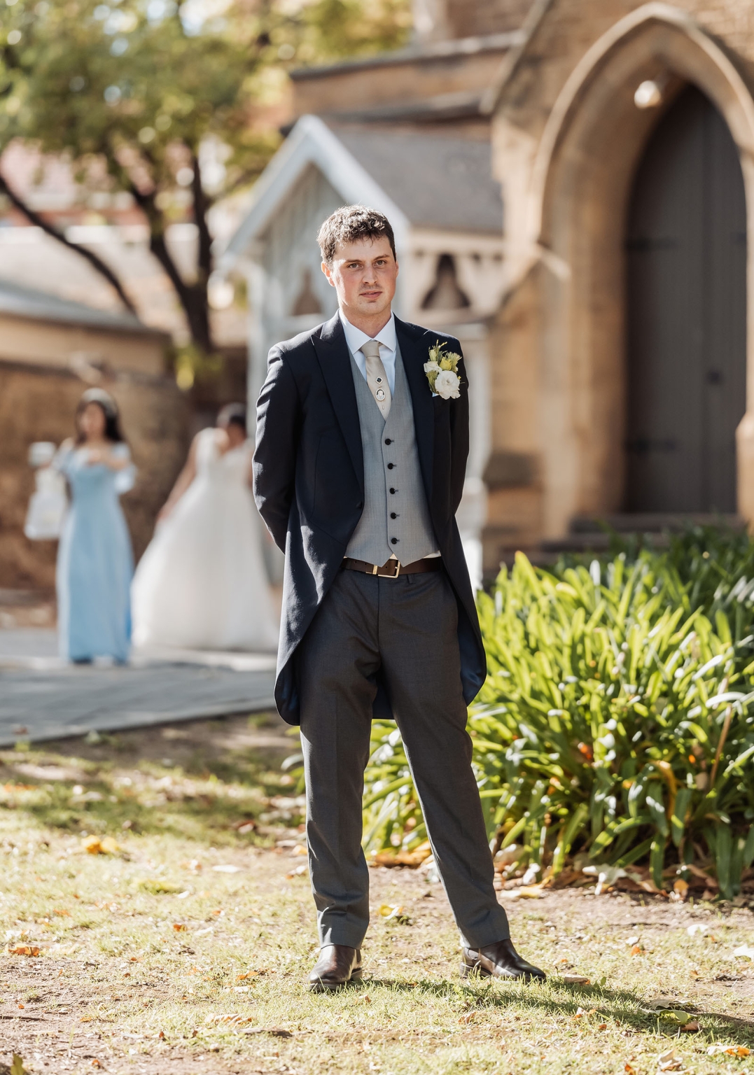 adelaide's st peter's cathedral wedding - irish & nick 5 Groom portrait outside stone church with bride blurred in background.