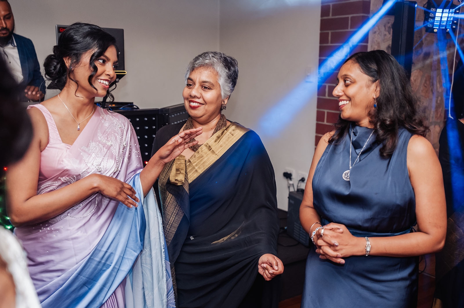 manor wedding in basket range - methmini & aravinda 172 Three women in vibrant traditional and modern attire engaged in joyful conversation at a celebration.