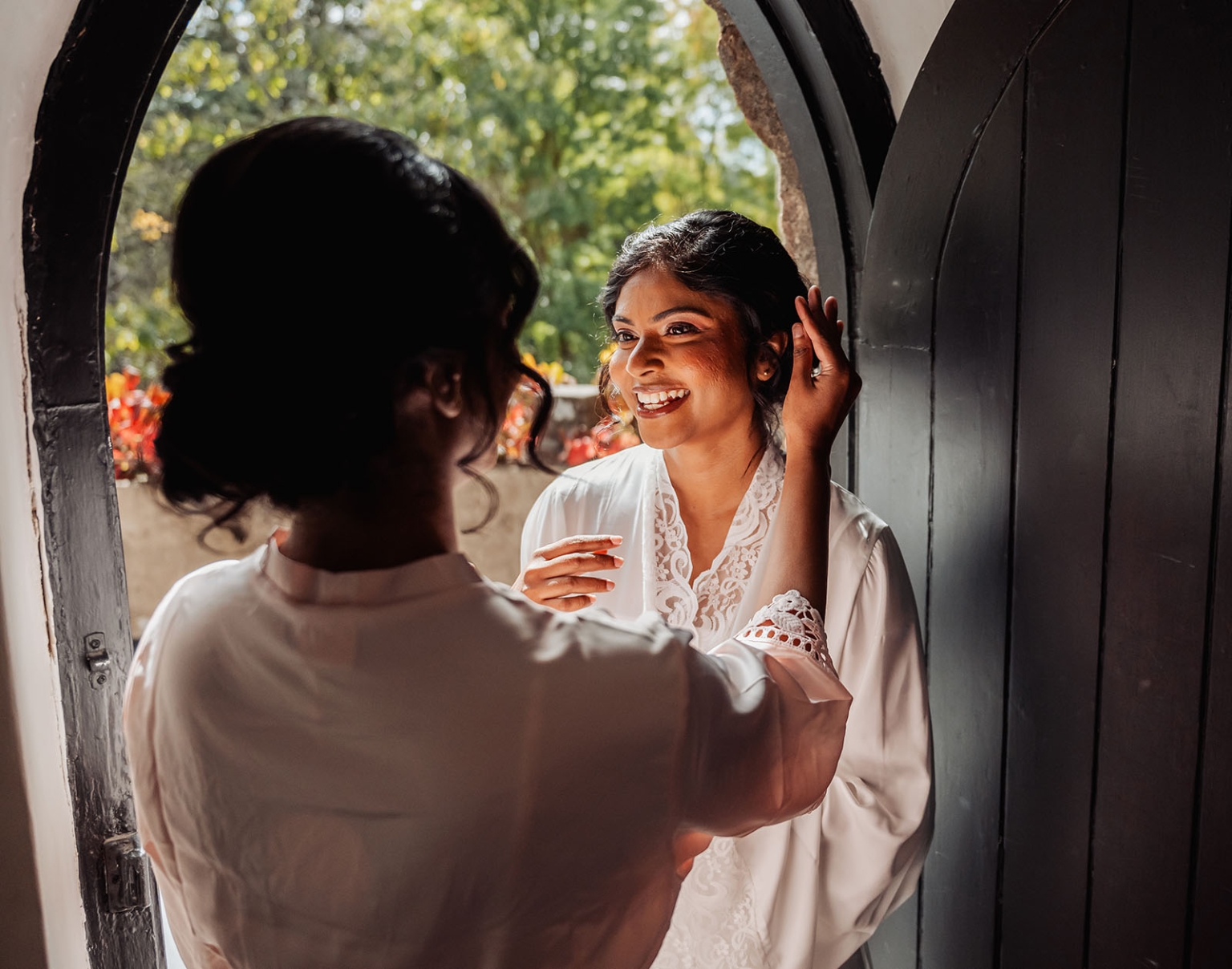 manor wedding in basket range - methmini & aravinda 112 Joyful woman in lace dress, standing by a sunlit doorway, sharing a happy moment.